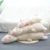Une image de trois peluches de licorne blanche et rose allongées sur un tapis et un canapé. Les peluches ont des cornes argentées et des ailes roses.