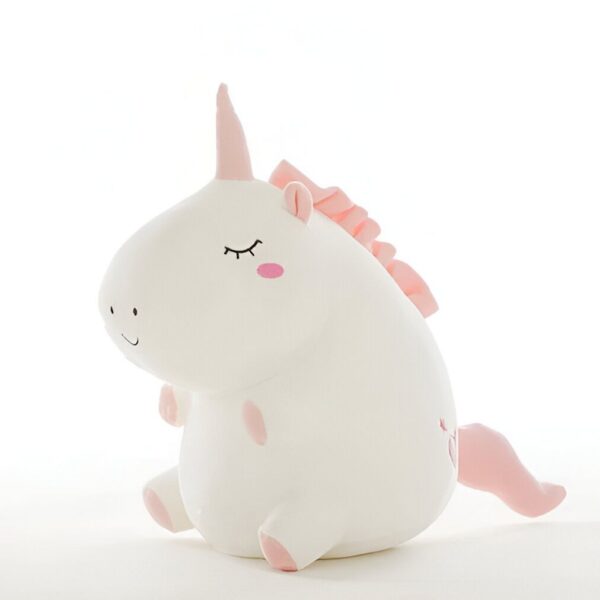 Une peluche licorne blanche et rose avec une crinière et une queue roses. La peluche est assise et a les yeux fermés.