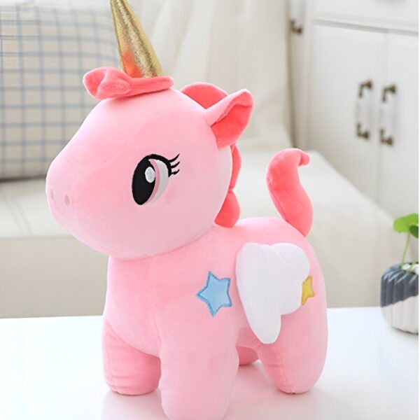 Une peluche rose en forme de licorne avec une corne dorée, des ailes blanches et des étoiles colorées.