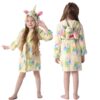 Une fillette porte un peignoir jaune à capuche avec motif de licorne. Le peignoir a une ceinture et des oreilles de licorne sur la capuche. La fillette est visible de face et de dos., 45502045880575,45502045913343,45502045946111,45502045978879,45502046011647,45502046044415,45502046077183,45502046109951 | Licorne Shop