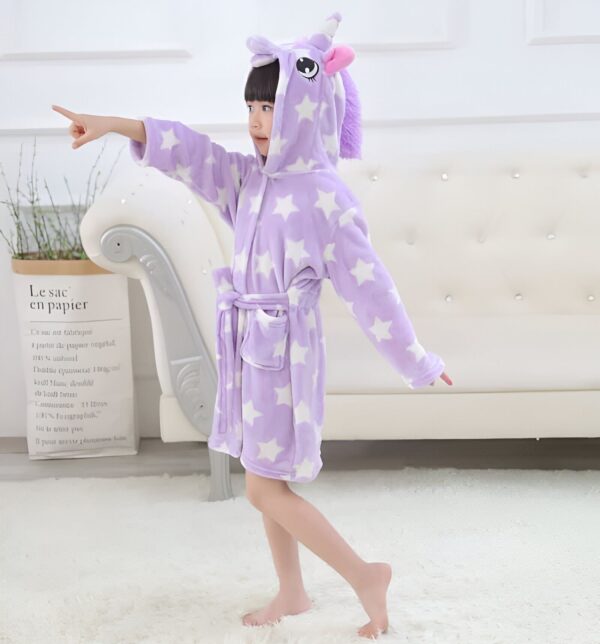 Enfant portant un peignoir en forme de licorne violet avec des étoiles blanches, souriant et pointant du doigt, posant devant un canapé blanc., 45502026580223,45502026612991,45502026645759,45502026678527,45502026711295,45502026744063,45502026776831,45502026809599 | Licorne Shop