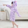Enfant portant un peignoir en forme de licorne violet avec des étoiles blanches, souriant et pointant du doigt, posant devant un canapé blanc., 45502026580223,45502026612991,45502026645759,45502026678527,45502026711295,45502026744063,45502026776831,45502026809599 | Licorne Shop