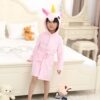 Une petite fille en peignoir rose licorne dans sa chambre. Un ourson en peluche et d'autres jouets sont sur le lit. Une coiffeuse blanche est visible en arrière-plan., 45502030971135,45502031003903,45502031036671,45502031069439,45502031102207,45502031134975,45502031167743,45502031200511 | Licorne Shop