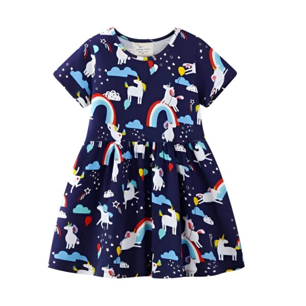 Une petite fille porte une robe bleue à motifs de licornes, de nuages et d'arcs-en-ciel. La robe a des manches courtes et une jupe évasée. La petite fille a les cheveux blonds et les yeux bleus. Elle est souriante et semble heureuse.