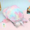 Un sac à dos en peluche de couleur arc-en-ciel avec une corne de licorne et des oreilles en 3D. Le sac à dos est ouvert et on peut voir l'intérieur qui est de couleur rose. Il y a des pompons roses sur les fermetures éclair.