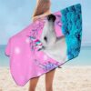 serviette-de-plage-motif-licorne-grande-taille-jumping-beans-1a.jpg Femme sur la plage enveloppée dans une serviette de plage à motif de tête de licorne blanche avec une corne colorée, des fleurs et des feuilles sur un fond rose et des fleurs bleues., 45501251944703 | Licorne Shop