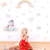 sticker-licorne-petite-fille-1a.jpg Une petite fille est assise par terre et regarde un sticker mural représentant une licorne assise sur un nuage. La licorne est blanche avec une crinière et une queue roses. Le nuage est rose et blanc. Il y a aussi un arc-en-ciel et des étoiles dans le sticker.
