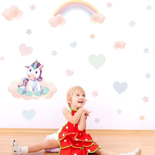 sticker-licorne-petite-fille-1a.jpg Une petite fille est assise par terre et regarde un sticker mural représentant une licorne assise sur un nuage. La licorne est blanche avec une crinière et une queue roses. Le nuage est rose et blanc. Il y a aussi un arc-en-ciel et des étoiles dans le sticker.