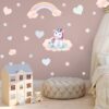 sticker-licorne-petite-fille-2a.jpg Une chambre d'enfant avec une décoration de licorne. Il y a un lit, une maison de poupée, un pouf et des nuages, des étoiles et des cœurs en guise de décoration murale.