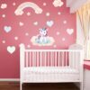sticker-licorne-petite-fille-3a.jpg Une chambre de bébé avec une licorne assise sur un nuage. Il y a un arc-en-ciel, des étoiles et des cœurs sur le mur. La chambre est peinte en rose.