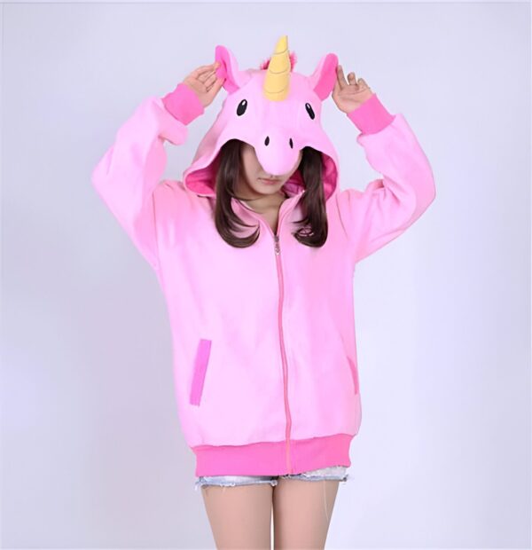 Jeune femme portant un sweat à capuche rose avec une tête de licorne et une corne jaune, les mains levées près de la tête., 45502396432639,45502396465407,45502396498175,45502396530943,45502396563711,45502396596479,45502396629247,45502396662015 | Licorne Shop