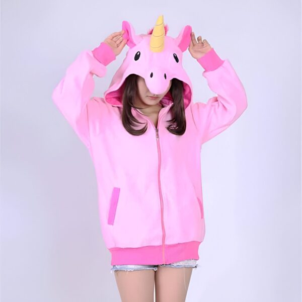 Jeune femme portant un sweat à capuche rose avec une tête de licorne et une corne jaune, les mains levées près de la tête., 45502396432639,45502396465407,45502396498175,45502396530943,45502396563711,45502396596479,45502396629247,45502396662015 | Licorne Shop