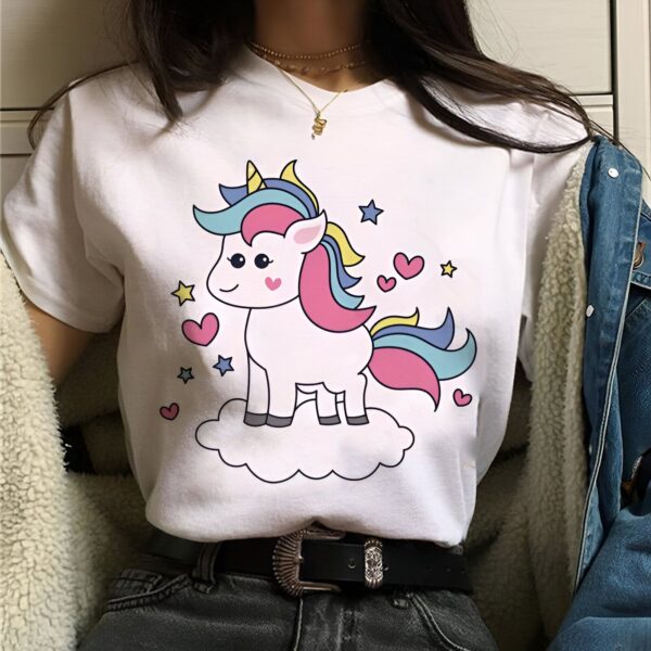 t-shirt-licorne-creature-unicorne-1a.jpg Une jeune femme porte un t-shirt blanc avec un dessin de licorne. La licorne est blanche avec une crinière et une queue arc-en-ciel. Elle est debout sur un nuage et est entourée d'étoiles et de cœurs.