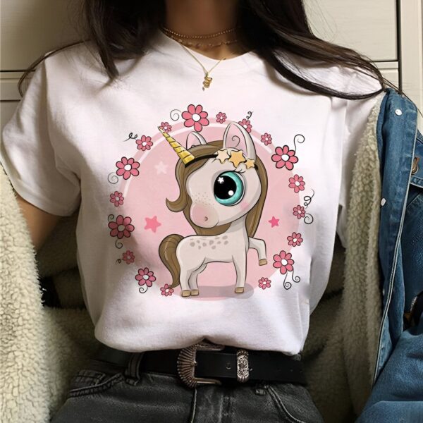 t-shirt-licorne-fleurs-1a.jpg Une jeune femme porte un t-shirt blanc avec un motif de licorne. La licorne est entourée de fleurs et d'étoiles.