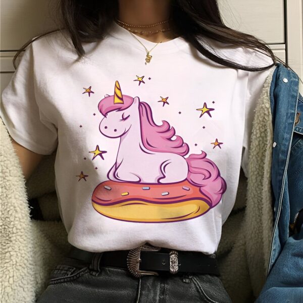 t-shirt-licorne-patisserie-1a.jpg Une illustration d'une licorne rose et blanche assise sur un beignet rose et jaune. La licorne a les yeux fermés et il y a des étoiles jaunes et roses autour d'elle.