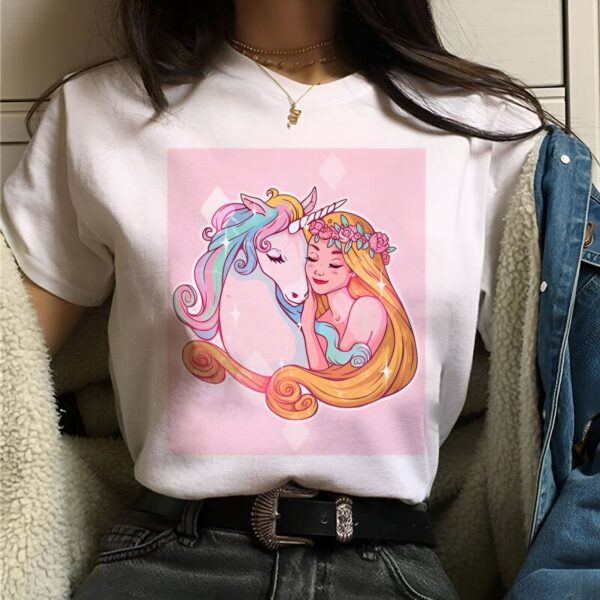 t-shirt-licorne-princesse-mignonne-1a.jpg Une jeune fille aux cheveux longs et blonds serre une licorne blanche dans ses bras. La licorne a une crinière et une queue arc-en-ciel. La fille porte une couronne de fleurs roses. Le fond est rose.