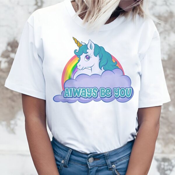 Une image d'une licorne avec une crinière verte et une corne jaune. La licorne est allongée sur un nuage devant un arc-en-ciel. Le texte "Always be you" est écrit sur le nuage. La licorne porte un collier avec un pendentif en forme de cœur.