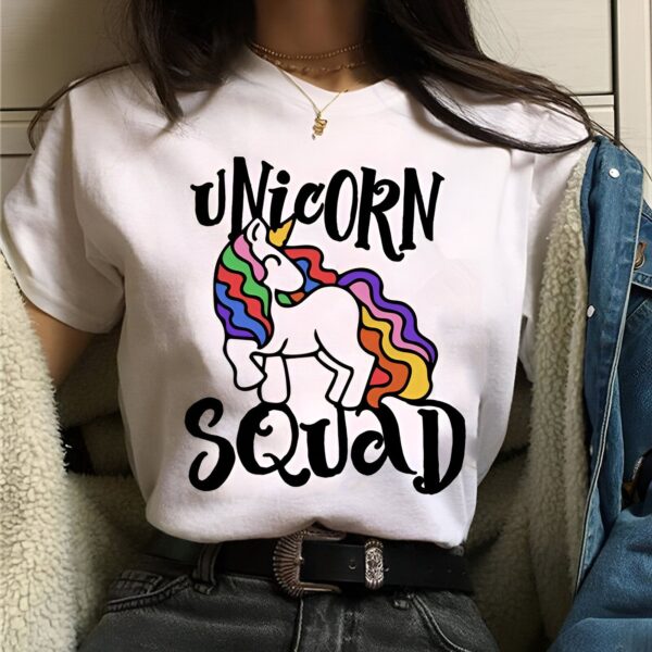 t-shirt-licorne-unicorn-squad-1a.jpg Une image d'une femme portant un t-shirt blanc avec le texte "Unicorn Squad" écrit dessus. La femme est vue de face et porte un jean bleu. Elle a les cheveux longs et bruns. La police du texte est noire et le texte est entouré d'un arc-en-ciel.