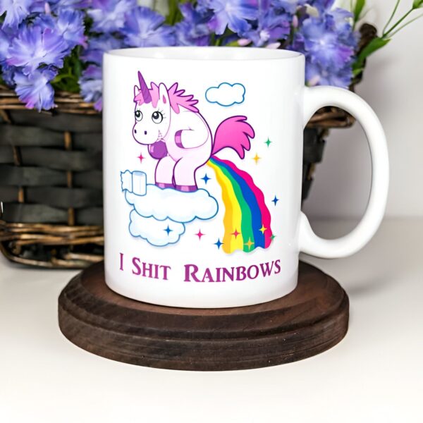 Mug blanc avec un dessin humoristique de licorne rose faisant des arcs-en-ciel sur un nuage. Inscription "I Shit Rainbows". Fleurs bleues en arrière-plan. Idée cadeau drôle., 45501199220991 | Licorne Shop