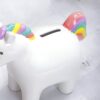 tirelire-licorne-enfant-en-ceramique-2a Une tirelire en céramique blanche en forme de licorne. La licorne a une crinière et une queue arc-en-ciel.