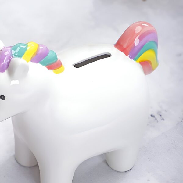 tirelire-licorne-enfant-en-ceramique-2a Une tirelire en céramique blanche en forme de licorne. La licorne a une crinière et une queue arc-en-ciel.