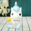 tirelire-licorne-mignonne-bleu-en-resine-1a.jpg Une tirelire en forme de licorne blanche et bleue avec une crinière et une queue arc-en-ciel. La licorne est assise sur une table et tient un ballon en forme de cœur avec le mot "love" dessus.
