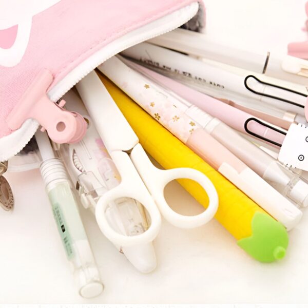 L'image montre une trousse rose en forme de chat ouverte avec des fournitures scolaires qui en sortent, notamment des stylos, des crayons, des ciseaux et des trombones.