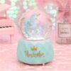 une-boule-a-neige-magique-licorne-bleue-1a.jpg Boule à neige féérique avec une figurine de licorne ailée à l'intérieur, posée sur un socle turquoise orné d'une couronne dorée et du mot "Unicorn" en lettres dorées. Un piano miniature rose et un vase décorent l'arrière-plan., 45501133521151 | Licorne Shop